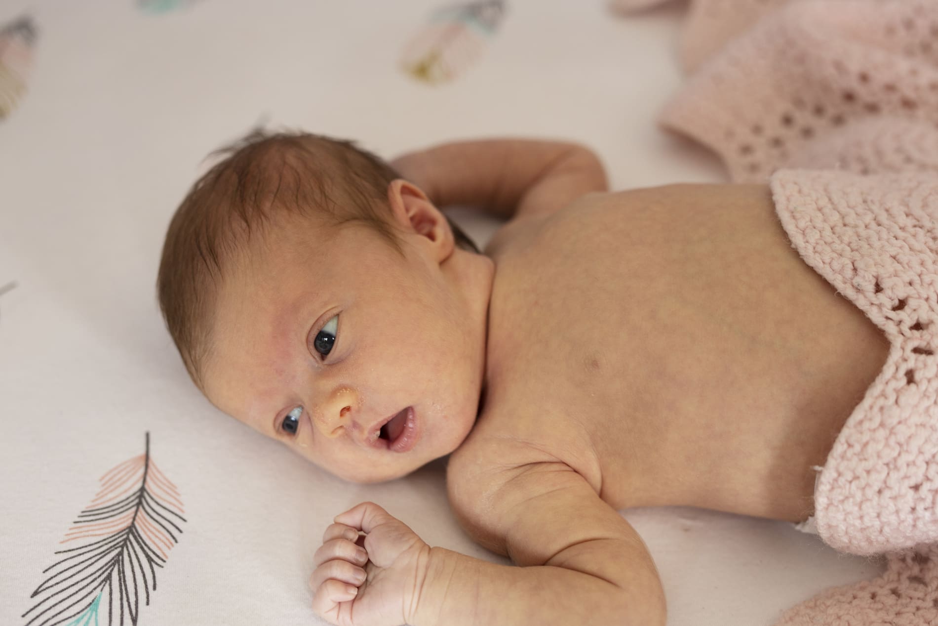 girl newborn baby lying in crib awake with pink blanket