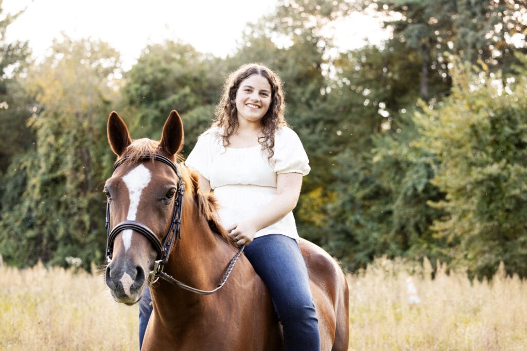 A girl on her horse in a field during her fall senior photo session in Chelmsford, Massachusetts