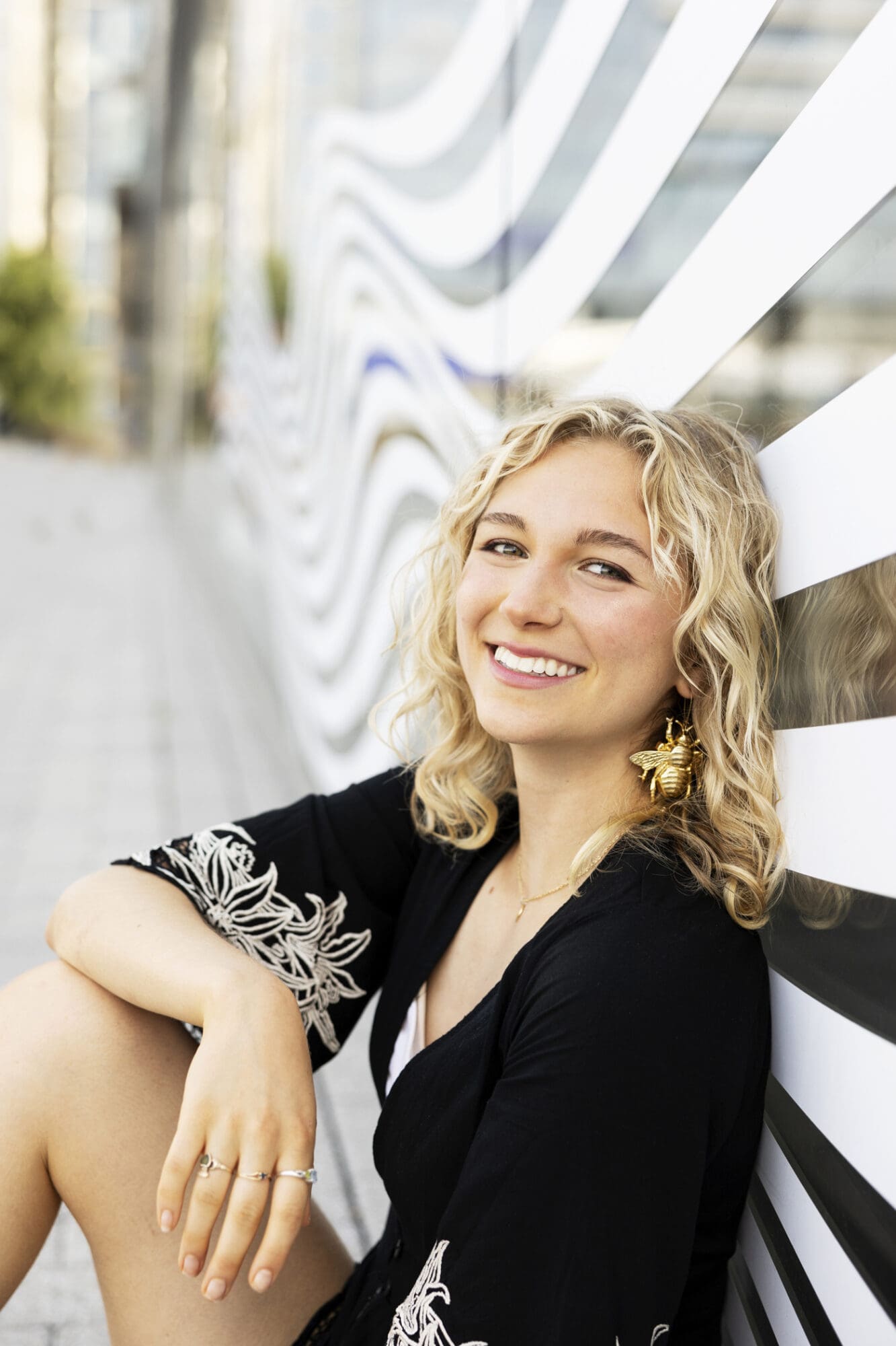 A senior girl smiles during her urban session in Boston Massachusetts, in front of a graphic black and white wall