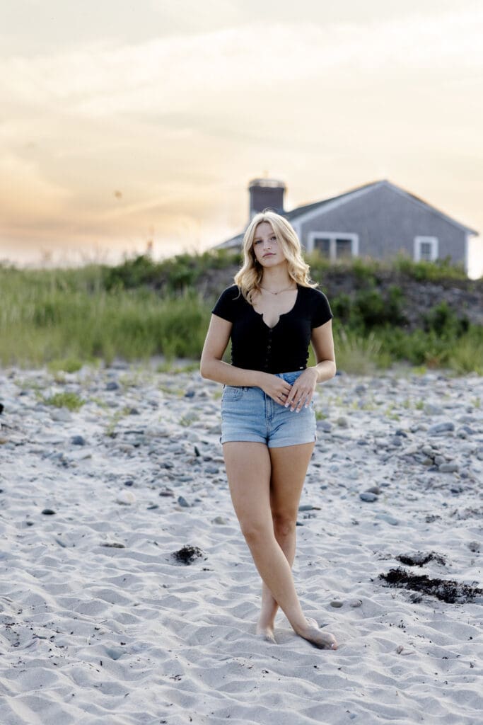 A senior girl walks on the beach in Massachusetts in denim shorts and bare feet
